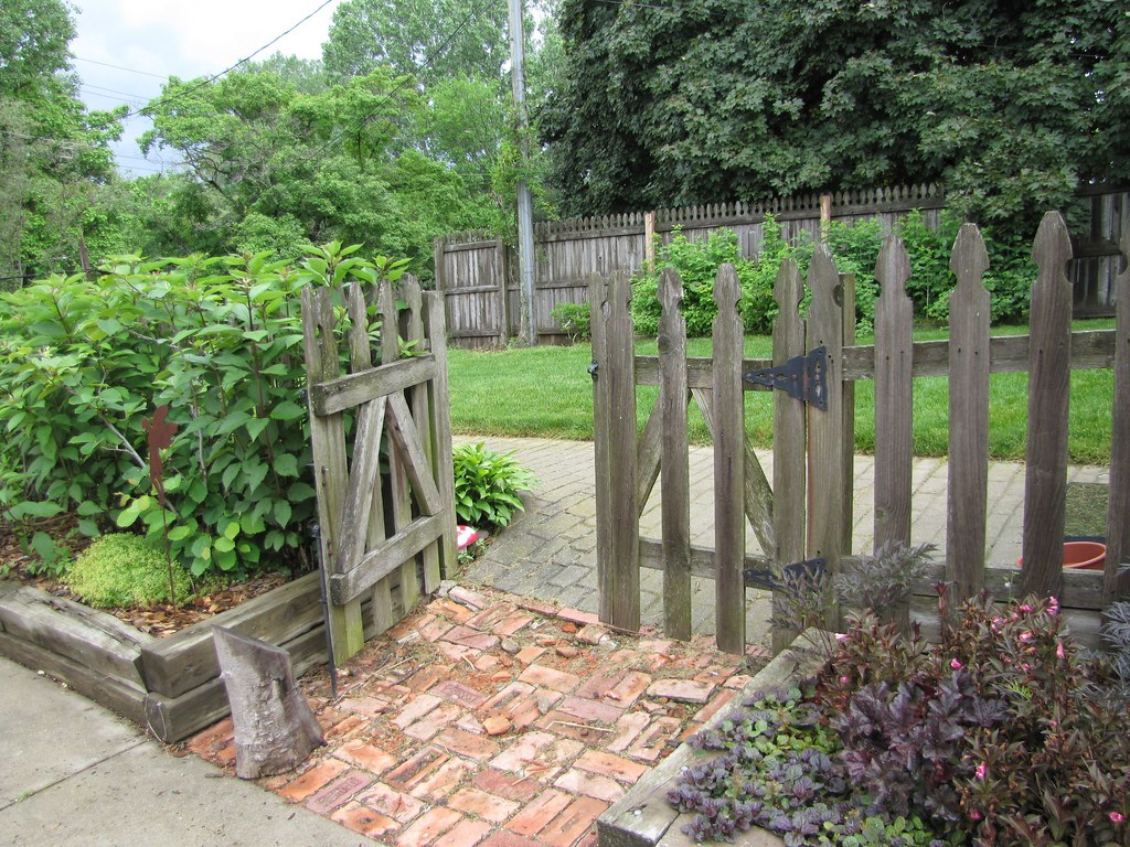 Weathered timber picket gate opening onto a brick garden path